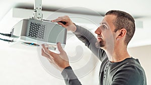 A man independently installs a multimedia video projector for a home theater or presentations on the ceiling