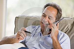 Man indoors using telephone looking at credit card
