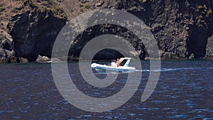Man on an inflatable runabout is floating along mountain of Lipari Island, Mediterranean sea. Summer sunny day. Sicily