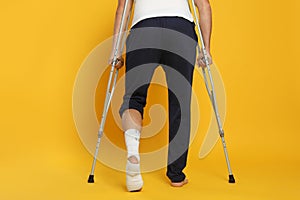 Man with injured leg using crutches on yellow background, closeup