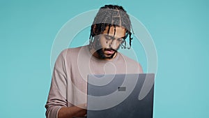 Man inputting data on laptop while standing in blue studio background