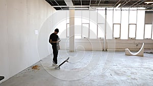 Man inside abandoned factory building is checking his mobile phone while playing with his skateboard and doing some tricks