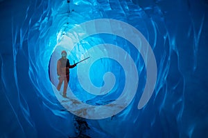 Man inside a melting glacier ice cave. Cut by water from the melting glacier, the cave runs deep into the ice of the Matanuska