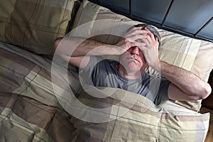 Man with insomnia lying in bed and snorting from exhaustion. photo