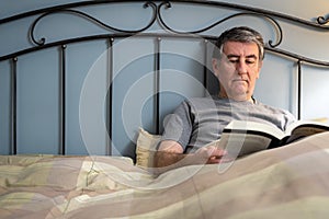 Man with insomnia sitting on the bed and reading a book.