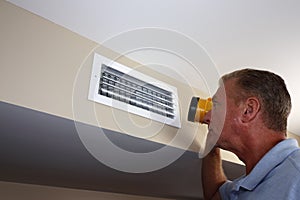 Man Inspecting a Home Rectangle Wall Air Vent with a Flashlight