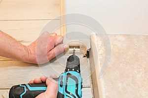 Man is installing the baseboard with a drill. Repair works indoors. Renovation in the flat