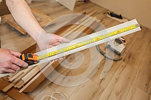 Man is installing the baseboard. Repair works indoors. Renovation in the flat.  Tape measure in hands