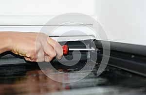 A man is installing a black plastic skirting board to a white wallpapered wall