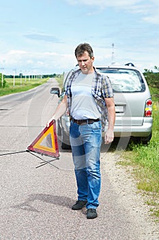 Man installing emergency sign on road near his car