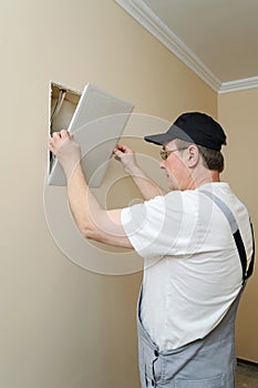 Man is installing hatch on the wall.