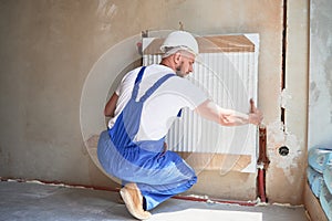 Man installing heating radiator in apartment under renovation.