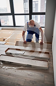 Man installing laminate flooring in apartment under renovation.