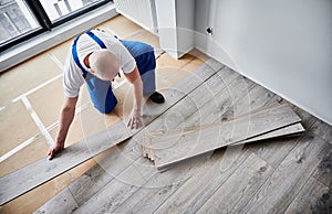 Man installing laminate wood flooring in apartment under renovation.