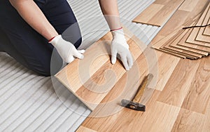 Man installing laminated floor, detail on wooden tile being fitted, over white foam base layer