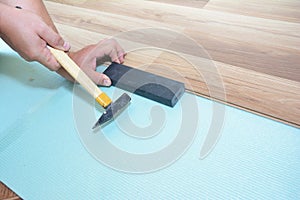 Man Installing New Laminate Wood Flooring. Worker Installing wooden laminate flooring with hammer. Handyman laying down laminate