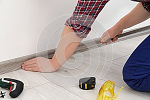 Man installing plinth on laminated floor in room