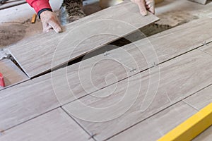 Man installing rectangular shaped floor tiles in kitchen. Applying adhesive before installation and verifying afterwards