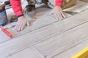 Man installing rectangular shaped floor tiles in kitchen. Applying adhesive before installation and verifying afterwards