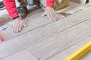 Man installing rectangular shaped floor tiles in kitchen. Applying adhesive before installation and verifying afterwards