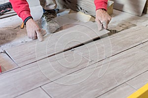 Man installing rectangular shaped floor tiles in kitchen. Applying adhesive before installation and verifying afterwards