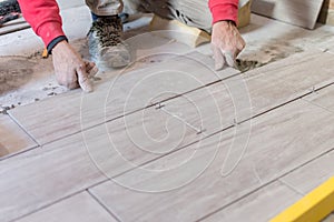 Man installing rectangular shaped floor tiles in kitchen. Applying adhesive before installation and verifying afterwards