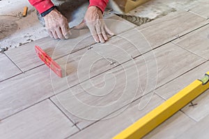 Man installing rectangular shaped floor tiles in kitchen. Applying adhesive before installation and verifying afterwards