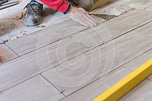 Man installing rectangular shaped floor tiles in kitchen. Applying adhesive before installation and verifying afterwards