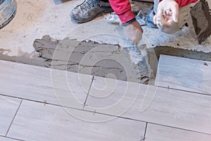 Man installing rectangular shaped floor tiles in kitchen. Applying adhesive before installation and verifying afterwards