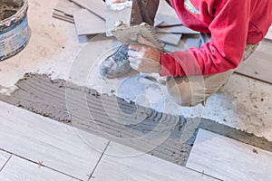 Man installing rectangular shaped floor tiles in kitchen. Applying adhesive before installation and verifying afterwards