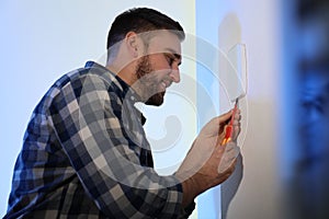 Man installing security alarm system on light wall at home