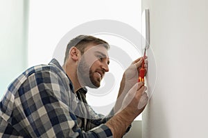 Man installing security alarm system on light wall at home