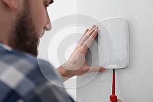 Man installing security alarm system on light wall at home, closeup