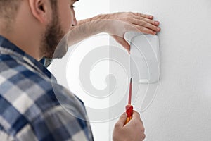 Man installing security alarm system on light wall at home, closeup