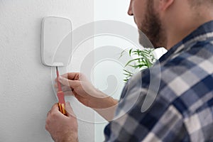 Man installing security alarm system on light wall at home, closeup