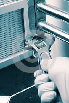 Man installing tightening a nut with a spanner wrench on a modern wall mounted radiator in a bathroom.