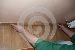 A man is installing a wooden oak skirting board to a wooden parquet flooring while room renovation and decoration