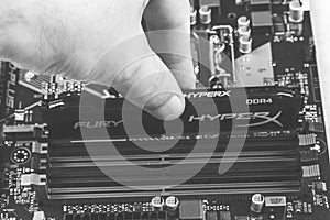 Man installs an DDR 4 DIMM 16 Gb Kingston HyperX Fury Memory RAM Module in the slot on the motherboard closeup, black and white ph