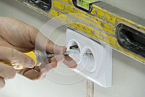 A man installs an electrical outlet in the wall. Close up of technician holding screwdriver near power socket. Electrician