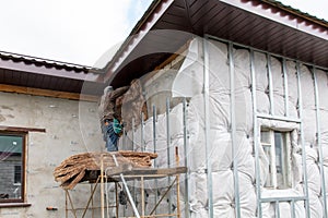 A man installs metal supports on the walls of the house for siding