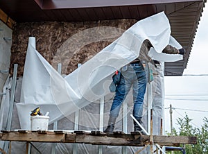 A man installs metal supports on the walls of the house for siding