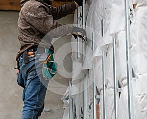 A man installs metal supports on the walls of the house for siding