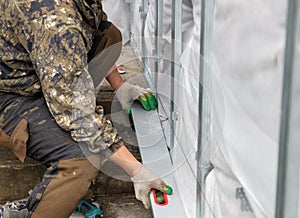 A man installs metal supports on the walls of the house for siding