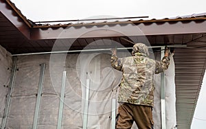 A man installs metal supports on the walls of the house for siding