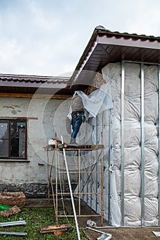 A man installs metal supports on the walls of the house for siding