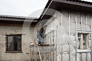 A man installs metal supports on the walls of the house for siding