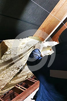 A man installs a thermal insulation layer of a thermal roof - using panels of mineral wool, mounting it between the beams of the