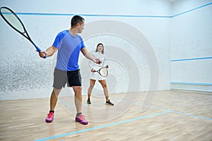 Man instructor fervently teaching woman to play squash exercising