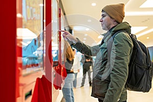 Man interacts with digital kiosk in modern mall, navigating touch screen. Technological integration into shopping photo