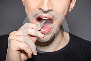 Man with interdental tooth brush hold handle into open mouth ready to clean space between teeth to prevent caries